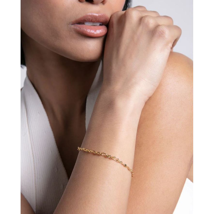 Elegant lady wearing a thin gold bracelet on her wrist, shown against a neutral background, showcasing delicate fashion jewelry style.