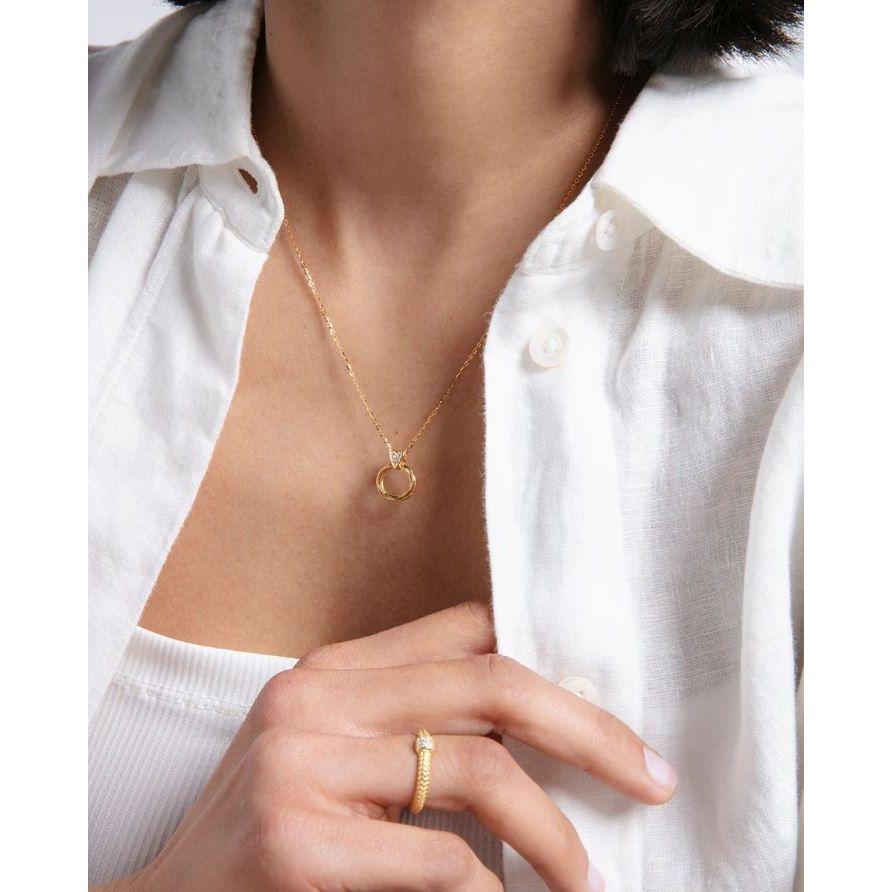 Woman wearing gold ring and necklace with white blouse, showcasing elegant jewelry style.