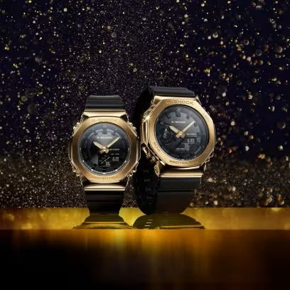 CASIO G-SHOCK Mod. OAK METAL COVERED OAK METAL COVERED - GOLD wristwatches with black resin straps on a gold glitter background