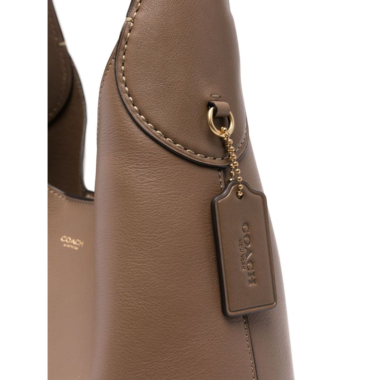 Close-up of light brown leather Coach Brooklyn leather hobo bag showing logo plaque and pendant detail.