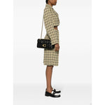 Coach Tabby shoulder bag in black leather with gold-tone hardware and chain strap worn by model in plaid outfit side view