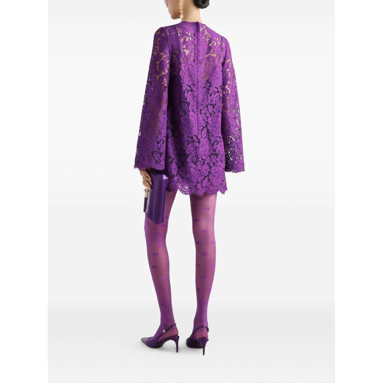 Woman wearing Dolce & Gabbana bell sleeves Lace mini dress in amethyst purple with rear zip and front tie, holding a clutch bag.