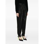 Woman wearing Iro Trousers Black with high waist, straight cut, and high-shine finish, styled with heels, showcasing side pockets detail.
