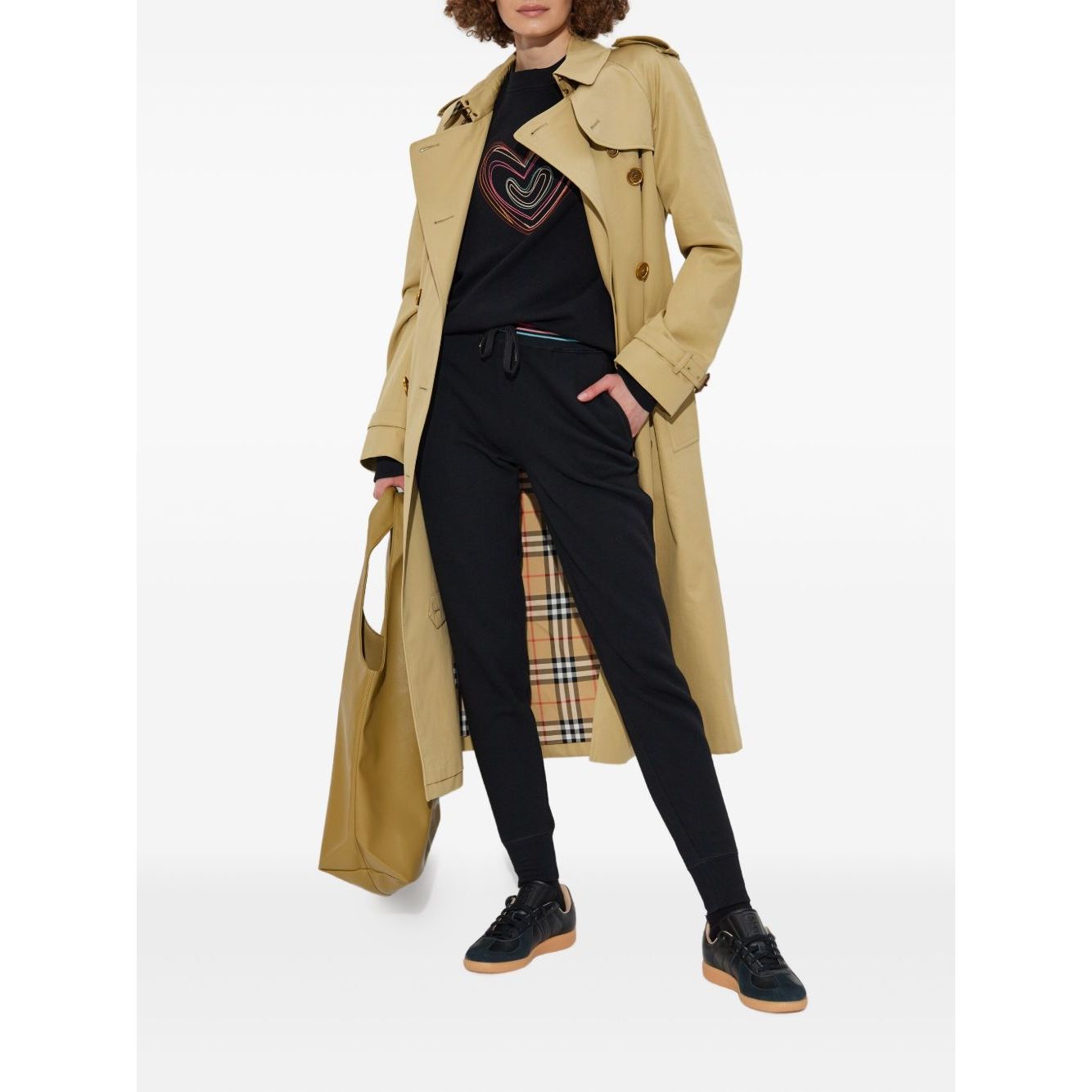 Model wearing PS By Paul Smith Sweaters Black with multicoloured heart, trench coat, and sneakers, showcasing relaxed fit and stylish look.