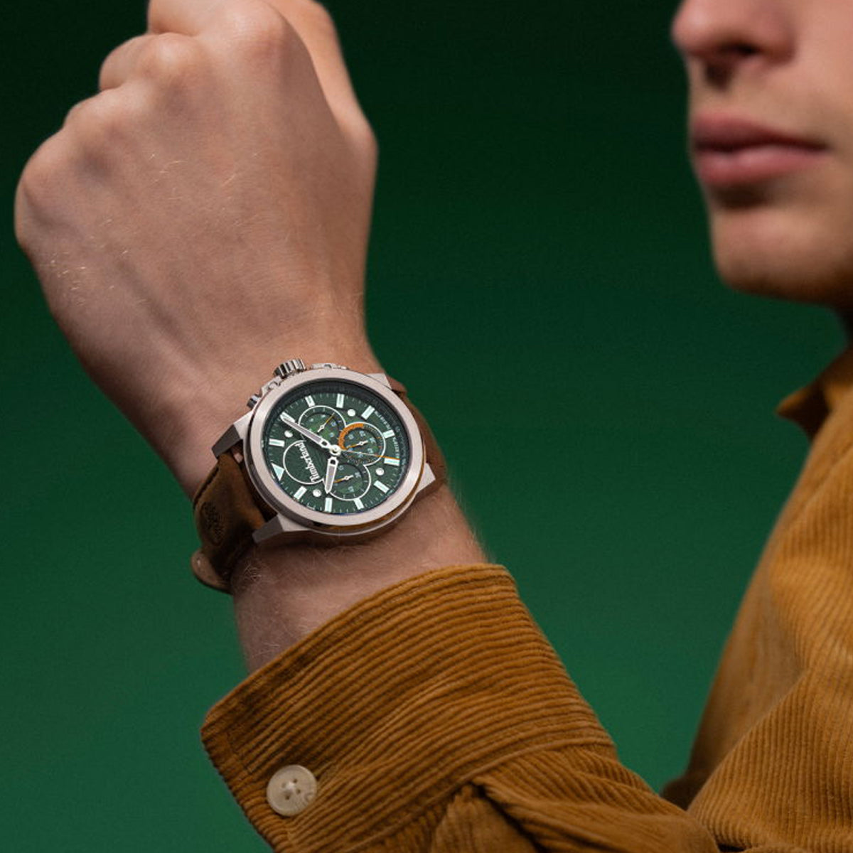 Man wearing wristwatch with brown strap and green dial on green background