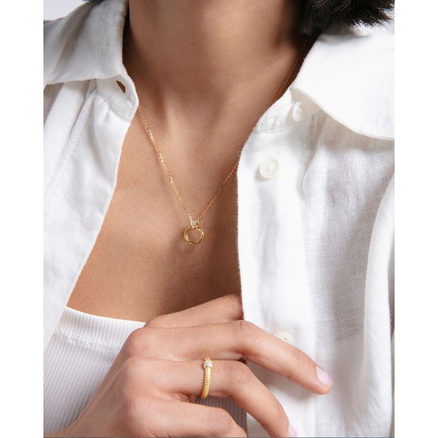 Woman wearing a gold necklace and ring, showcasing elegant accessories with a white shirt.